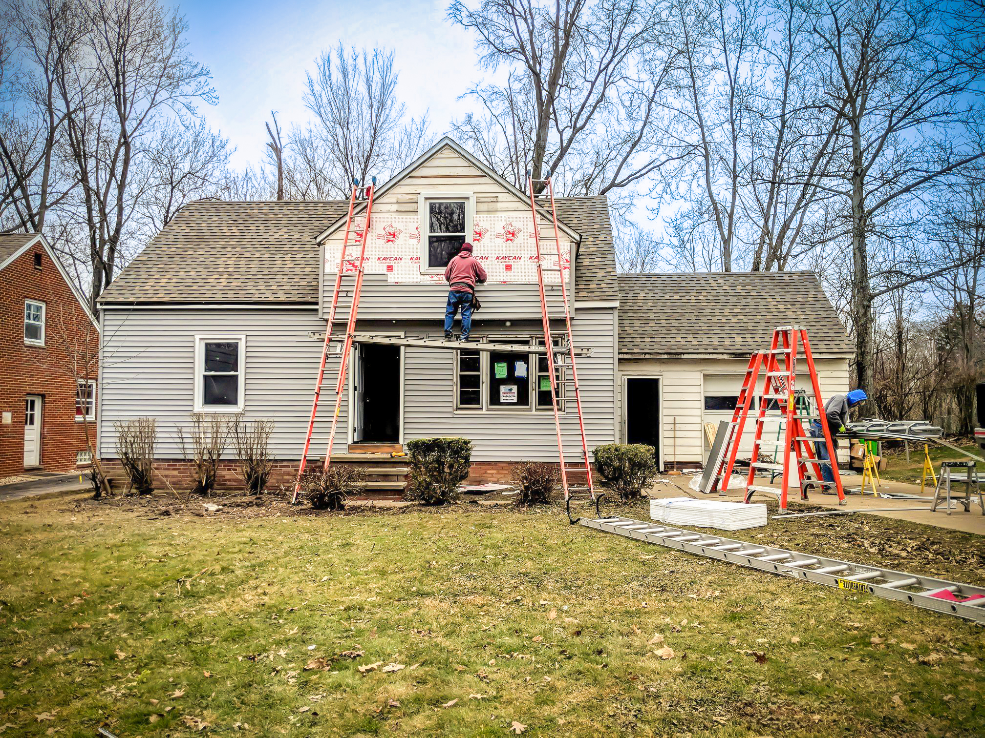 Landscape photograph of exterior single family house under renovation by skilled laborers.